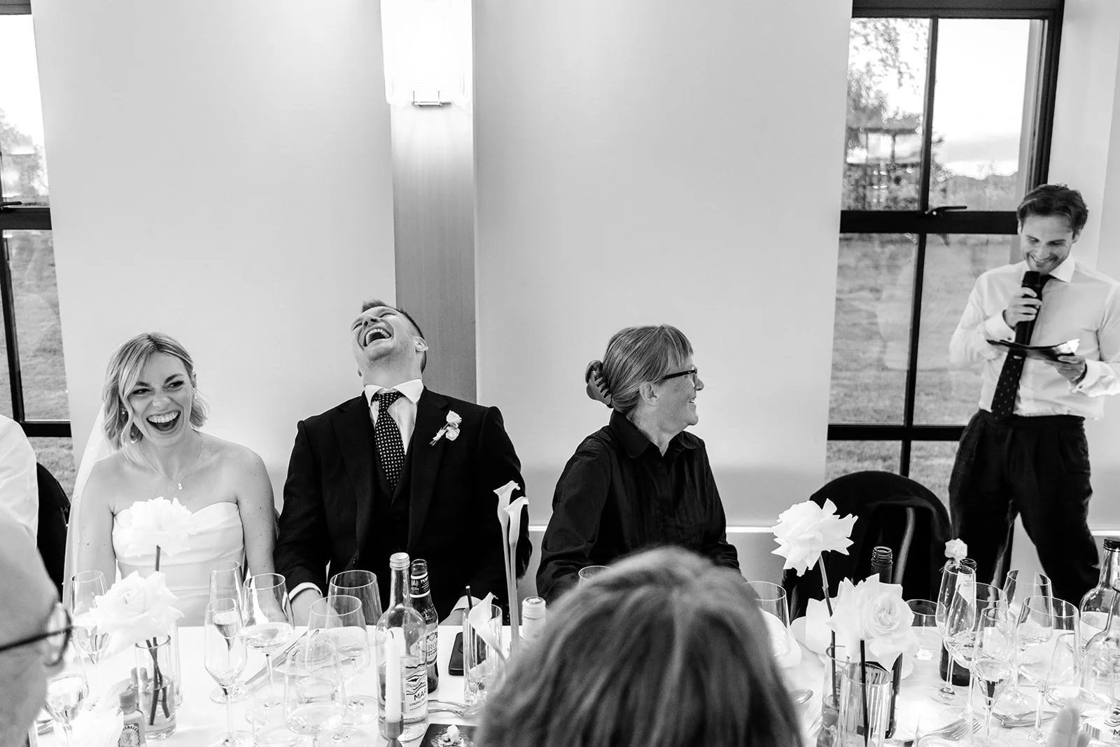The top table at Limekiln erupting in laughter during the speeches — Jack with his head thrown back, Abi beaming — black and white