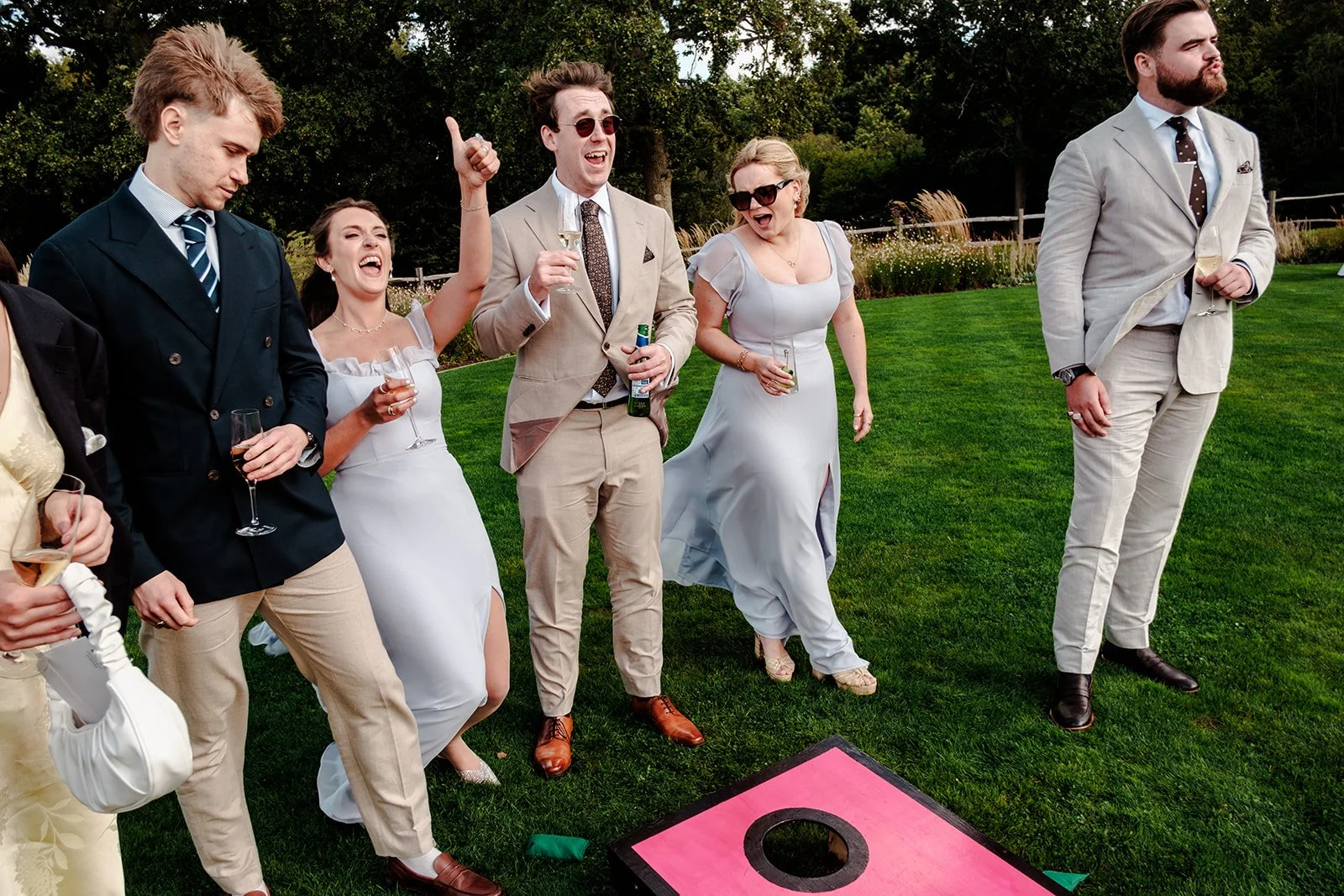 Guests playing cornhole lawn games on the beautifully kept Limekiln gardens during the drinks reception, bridesmaids in pale blue dresses