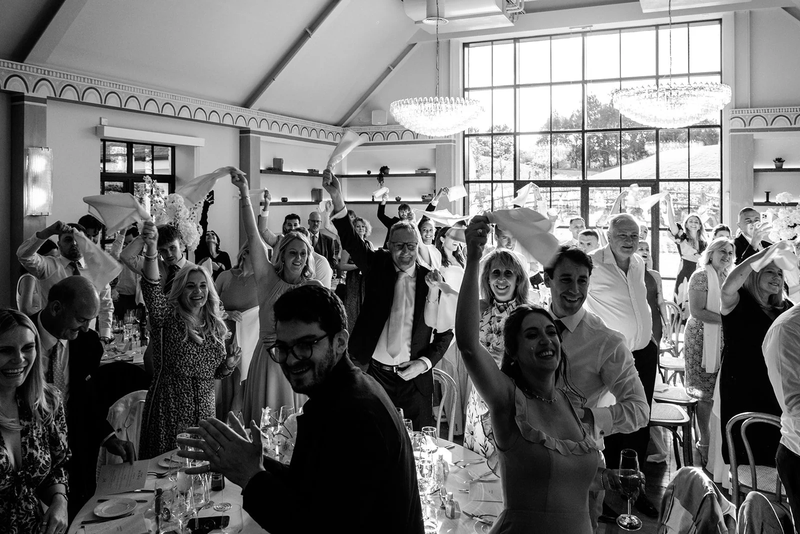 The whole room at Limekiln waving napkins and cheering during the speeches — pure wedding reception joy, black and white