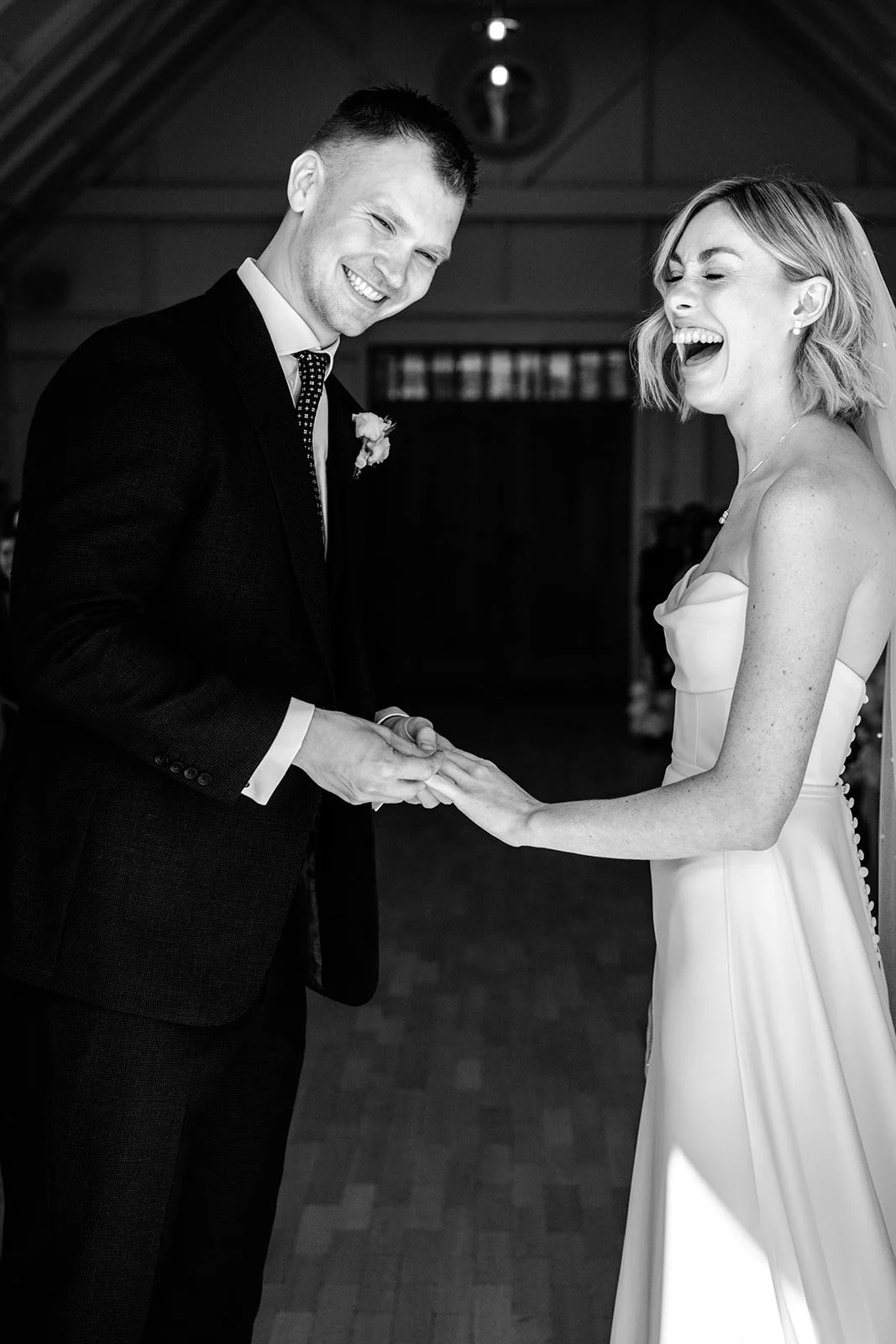 Jack and Abi both laughing during the ring exchange at their Limekiln wedding ceremony — pure, spontaneous joy, black and white