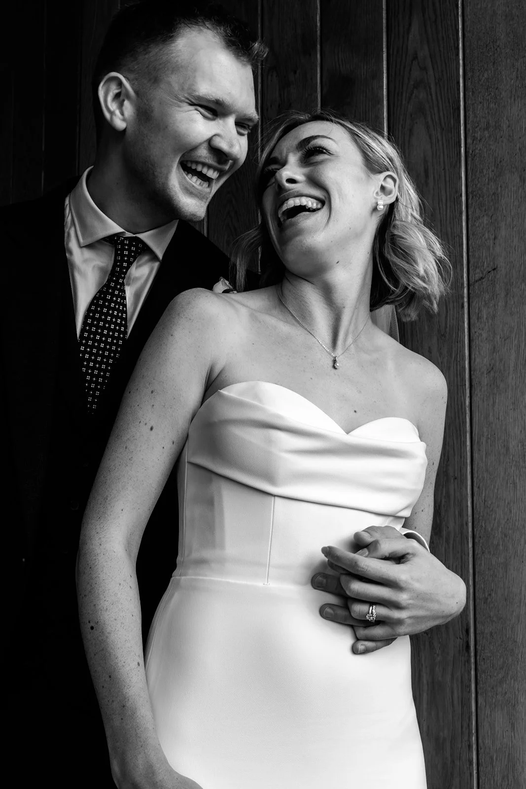 Intimate black and white portrait of Jack and Abi laughing together against the warm timber wall at Limekiln East Sussex
