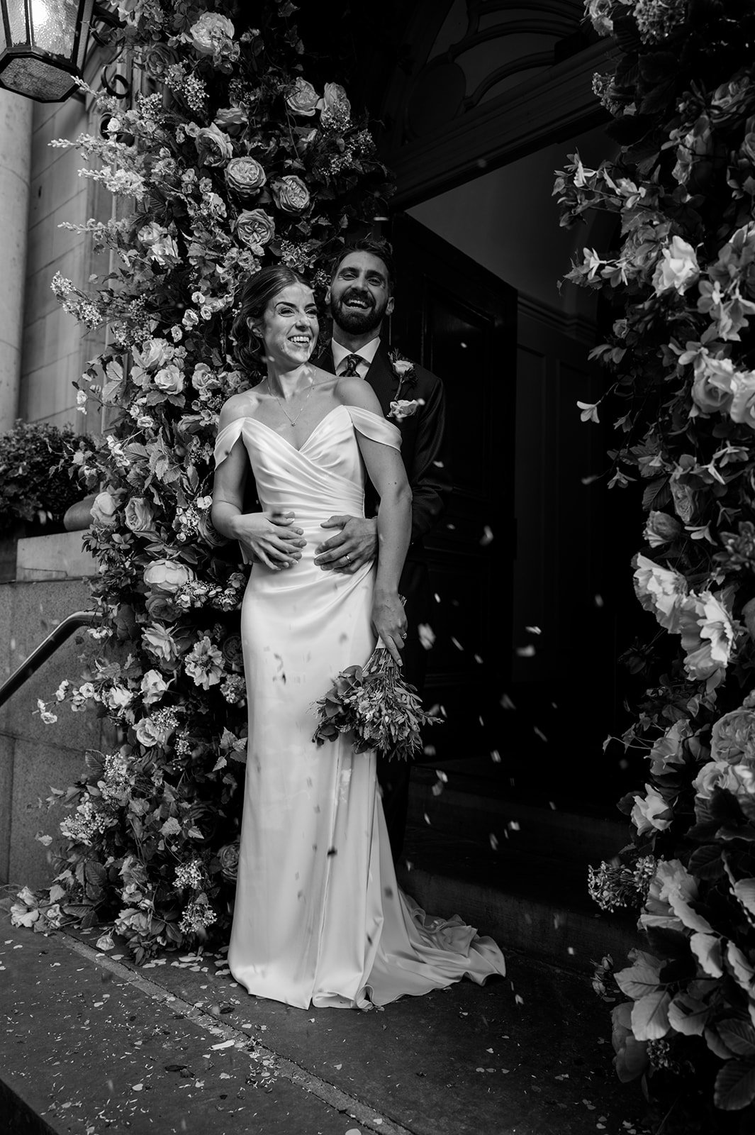 Bride and groom framed by the floral archway at the entrance to Chelsea Old Town Hall