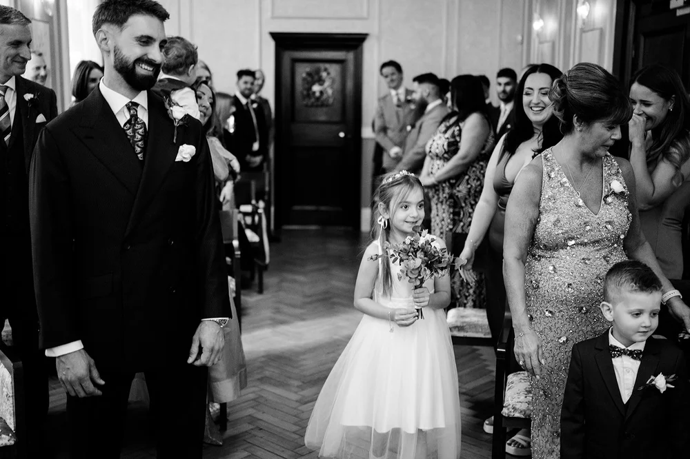 Groom and flower girl at the doors of Chelsea Old Town Hall as confetti falls