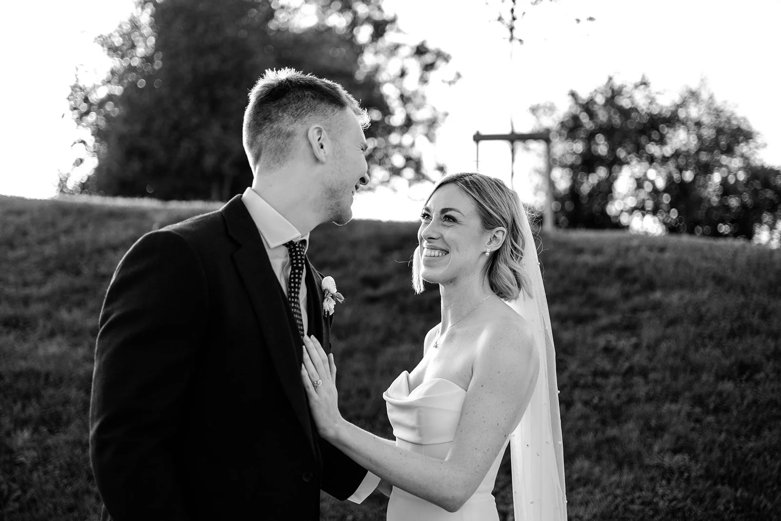 Jack and Abi at golden hour on the grassy hillside at Limekiln — Abi looking at Jack, both smiling softly, black and white