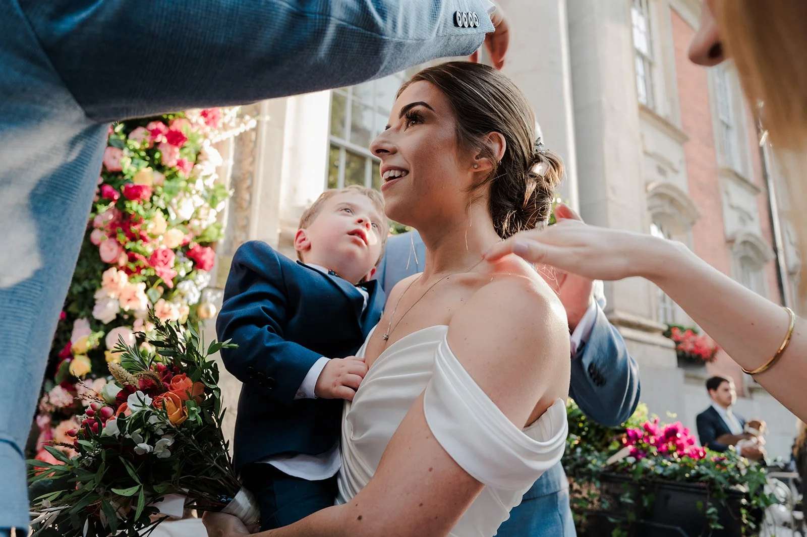 Nat holding a child outside Chelsea Town Hall with the floral arch behind
