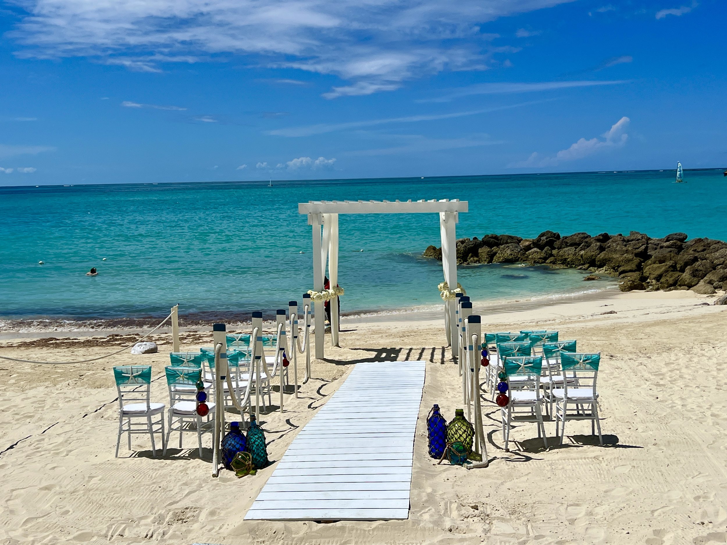 Beachfront Caribbean wedding ceremony setup with white arch and turquoise water in the background