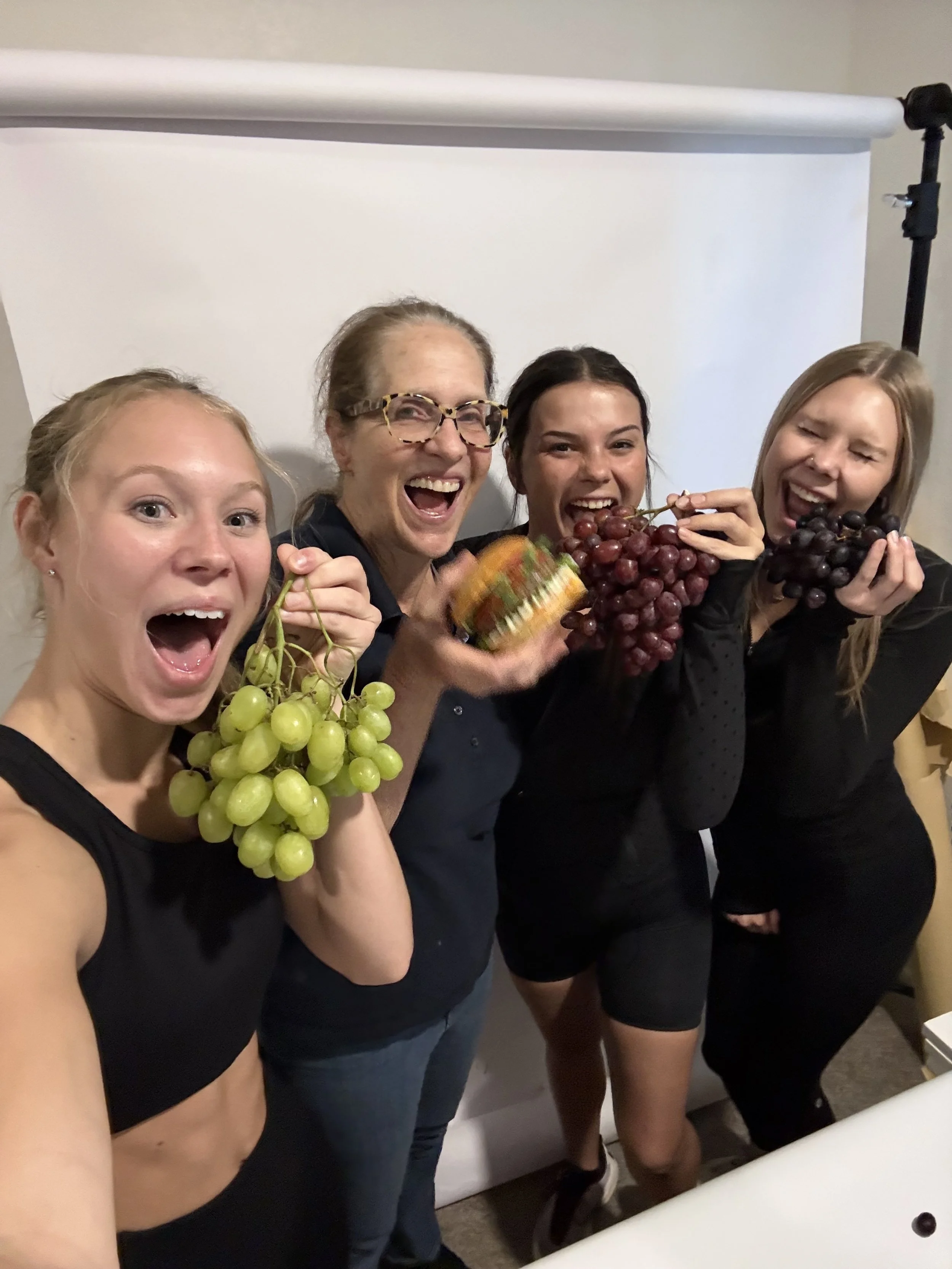 The studio crew on set during a content sprint, holding grapes in front of a white sweep