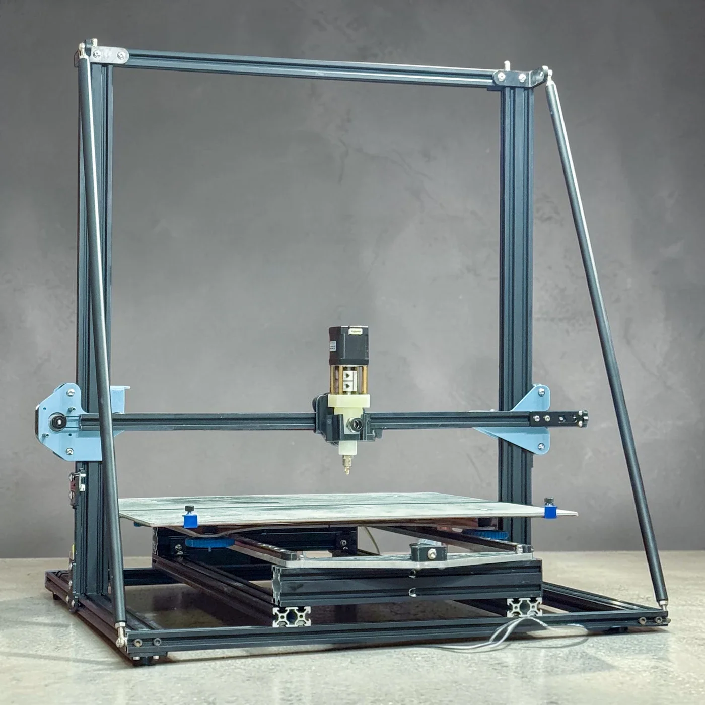 Large-format 3D printer with a broad build plate and central extrusion head.
