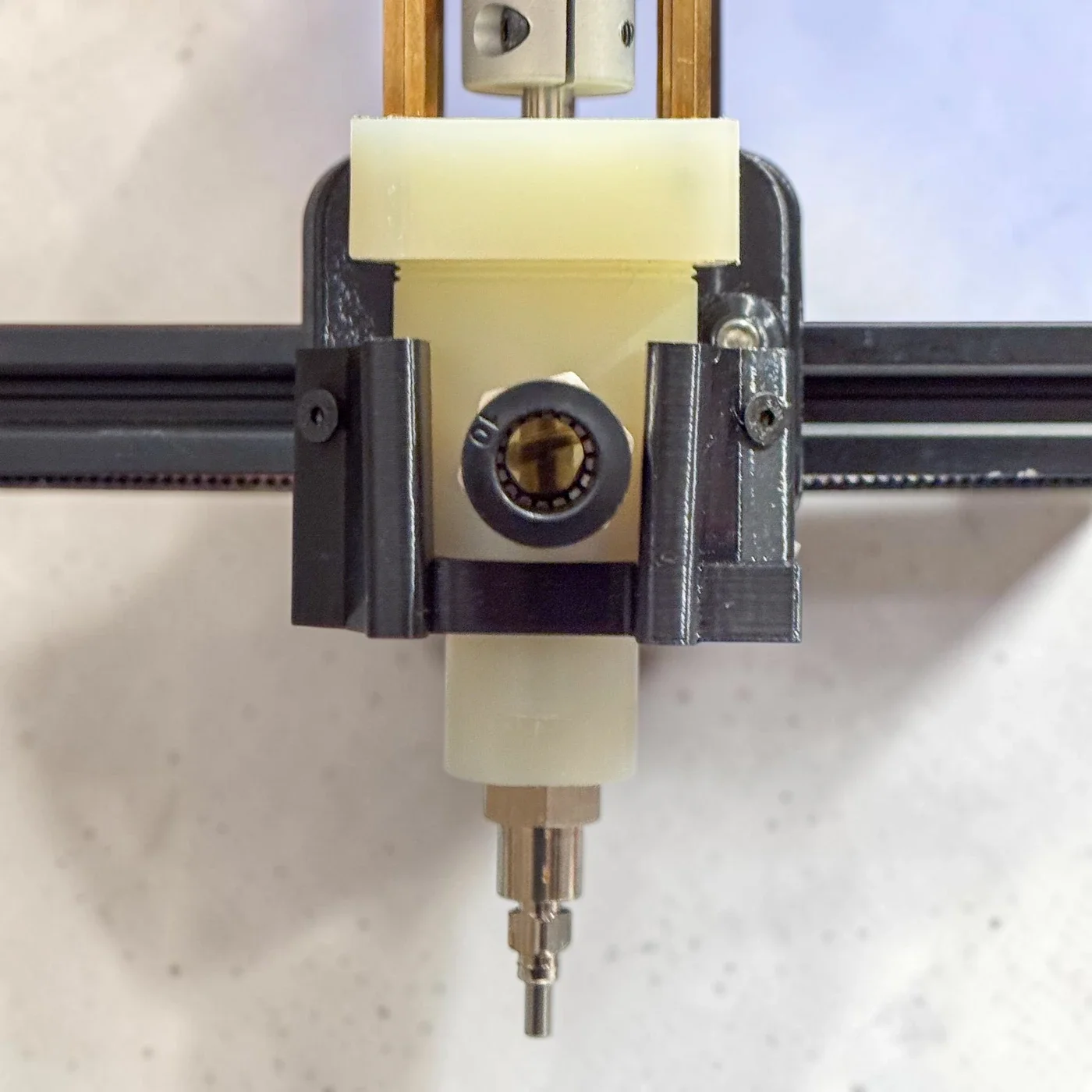Close view of the custom extrusion head and brass nozzle on the printer gantry.