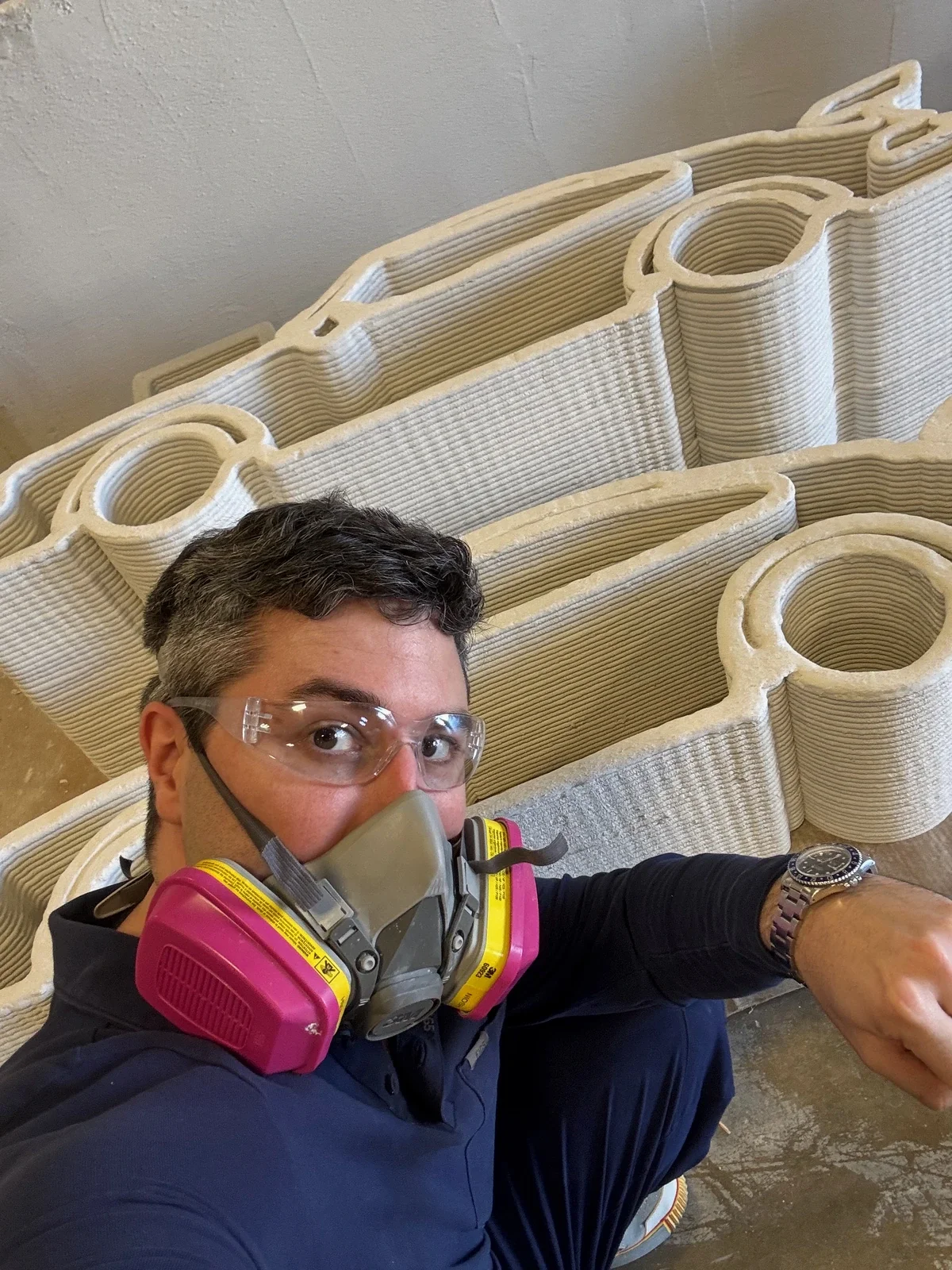 Rolando Guerra wearing safety glasses and a respirator beside a full-scale layered construction print.