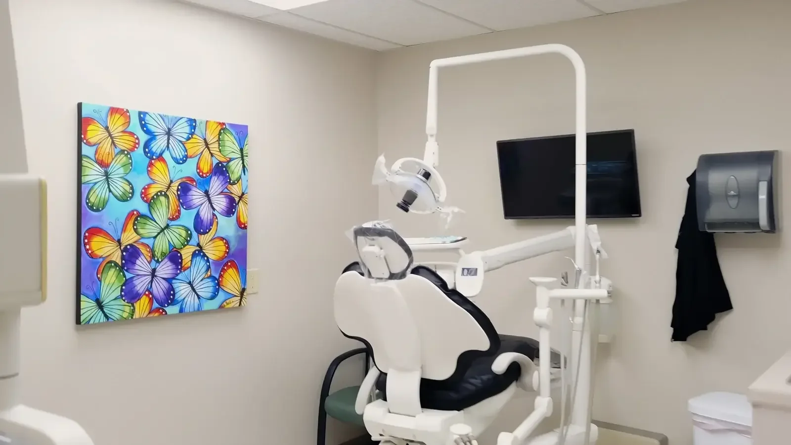 Empty dental operatory with a patient chair, overhead light and colorful butterfly artwork.