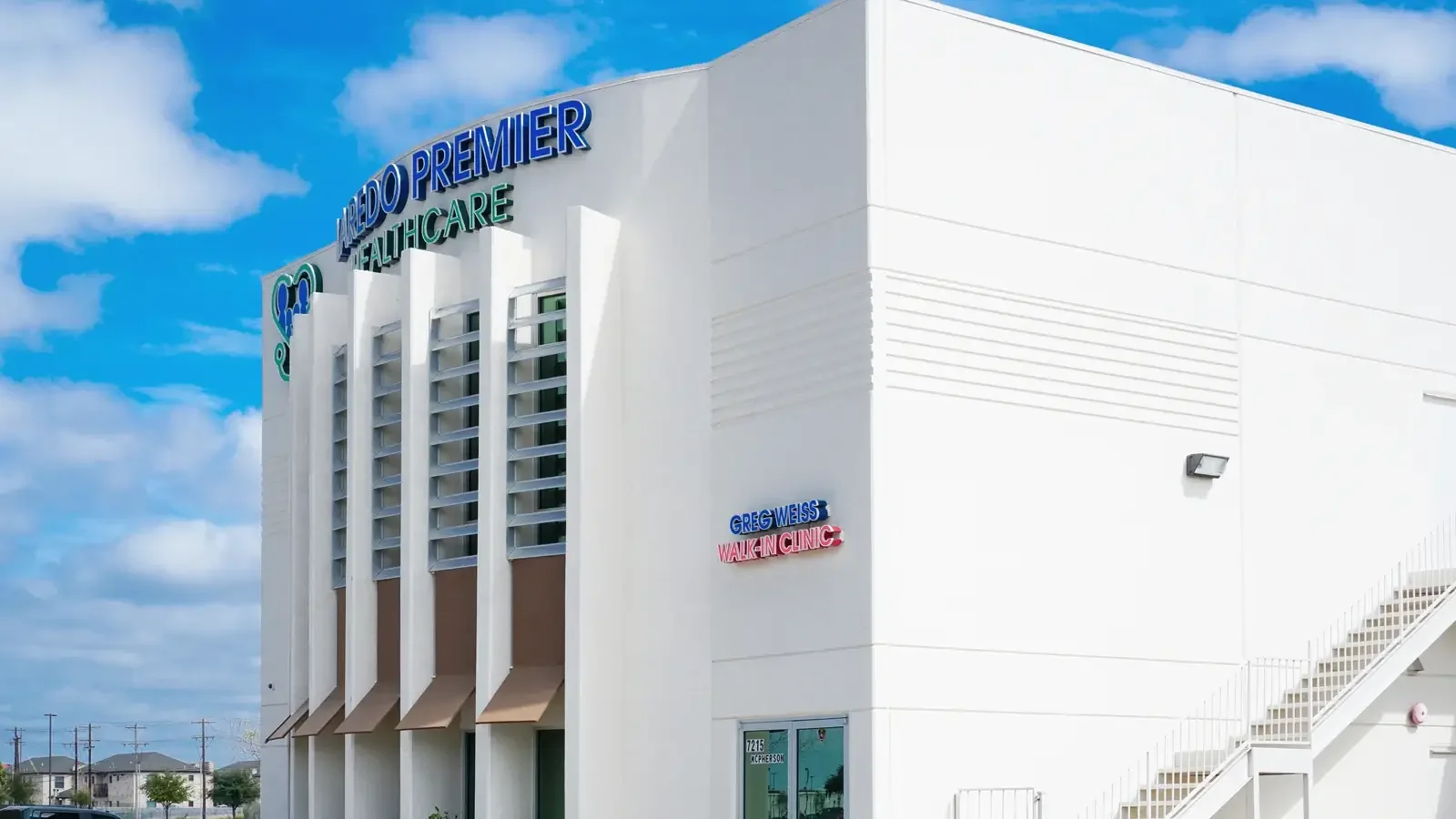 White Laredo Premier Healthcare building with blue and green facade signage under a blue sky.