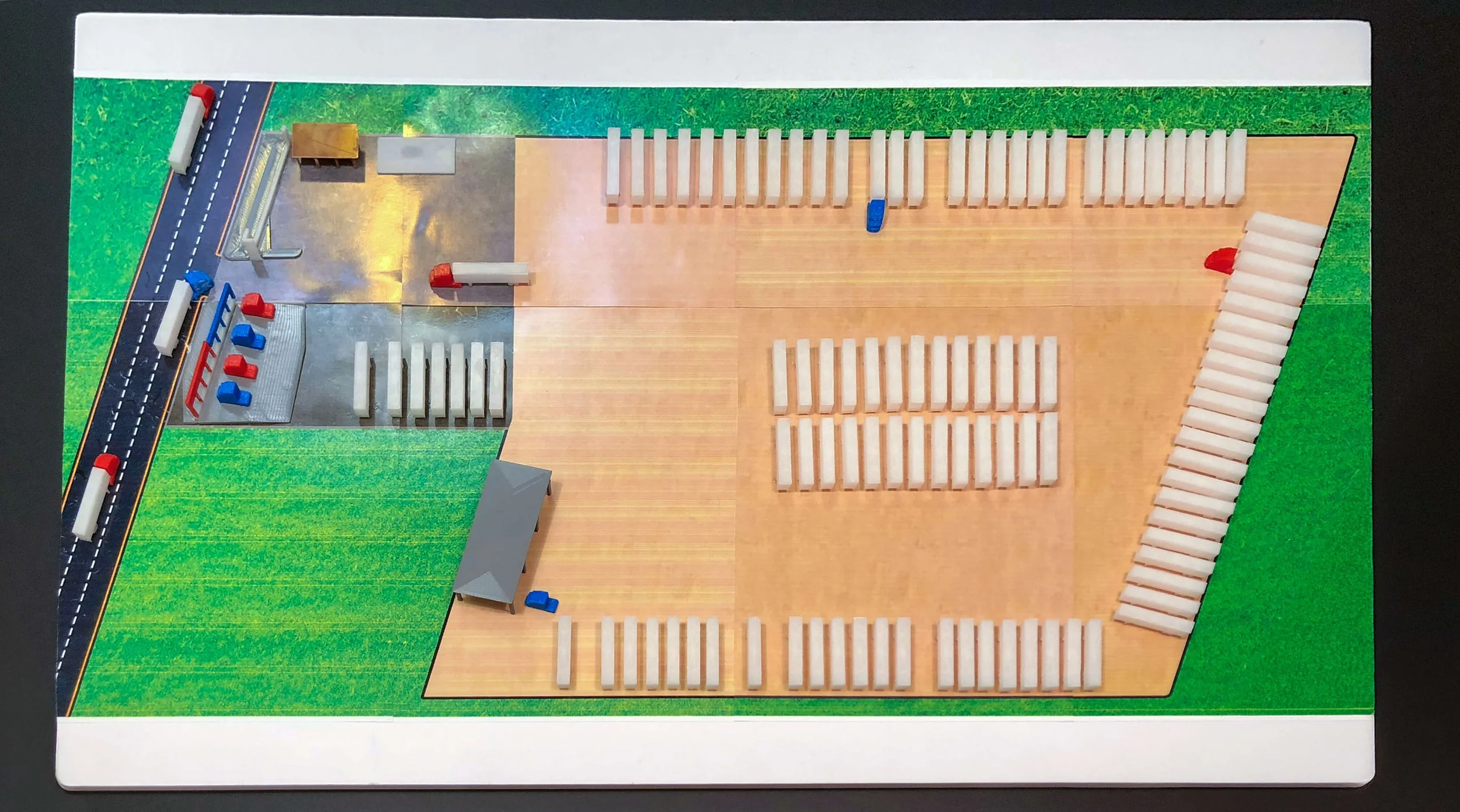 Overhead view of a tabletop truck-lot model with parking rows, roads, service buildings and small vehicles.