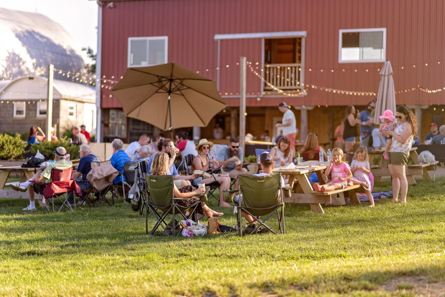 Families relaxing in lawn chairs on the grass outside the red barn