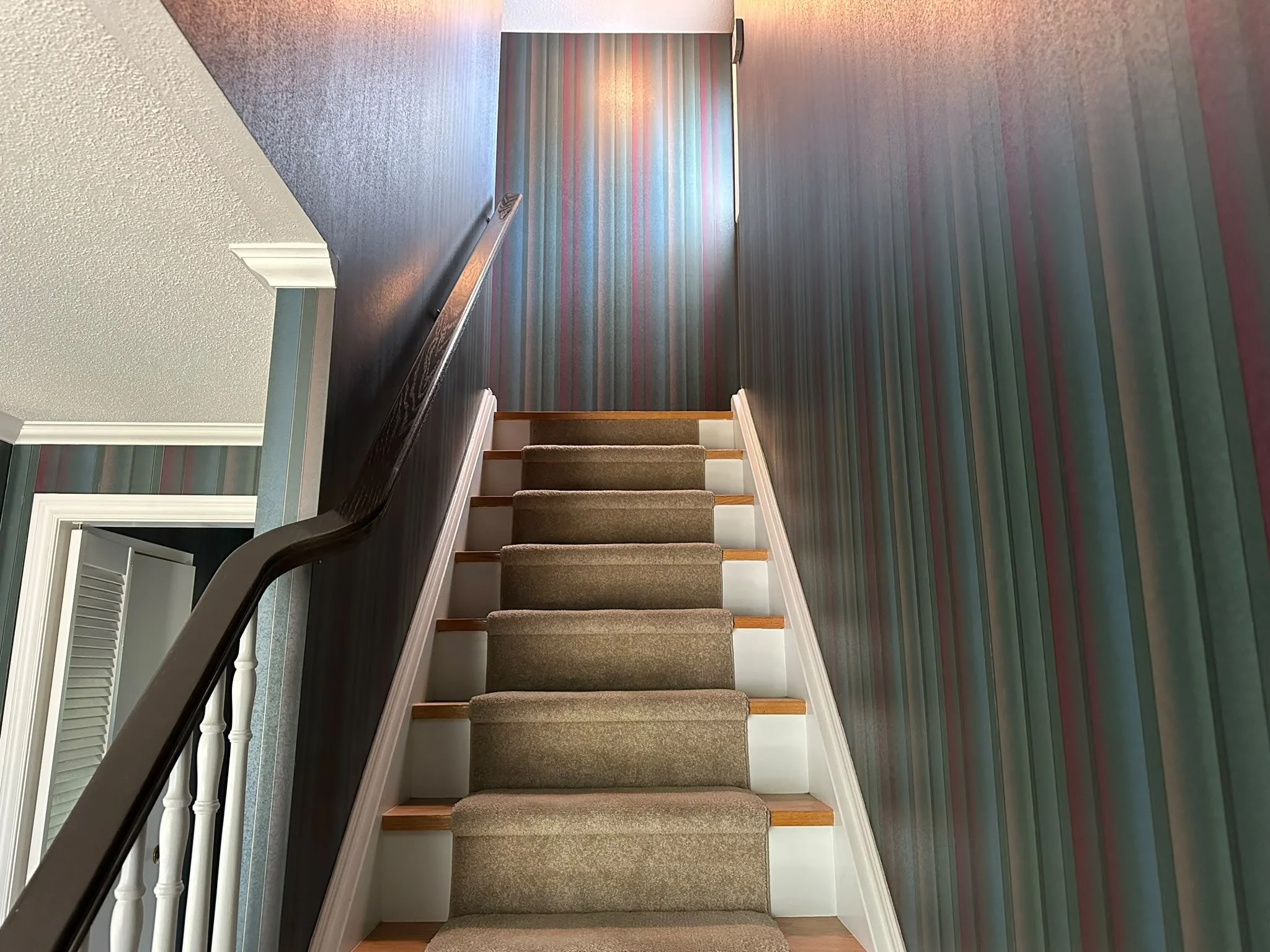 Before: striped wallpaper surrounding a staircase with a dark handrail and carpet runner