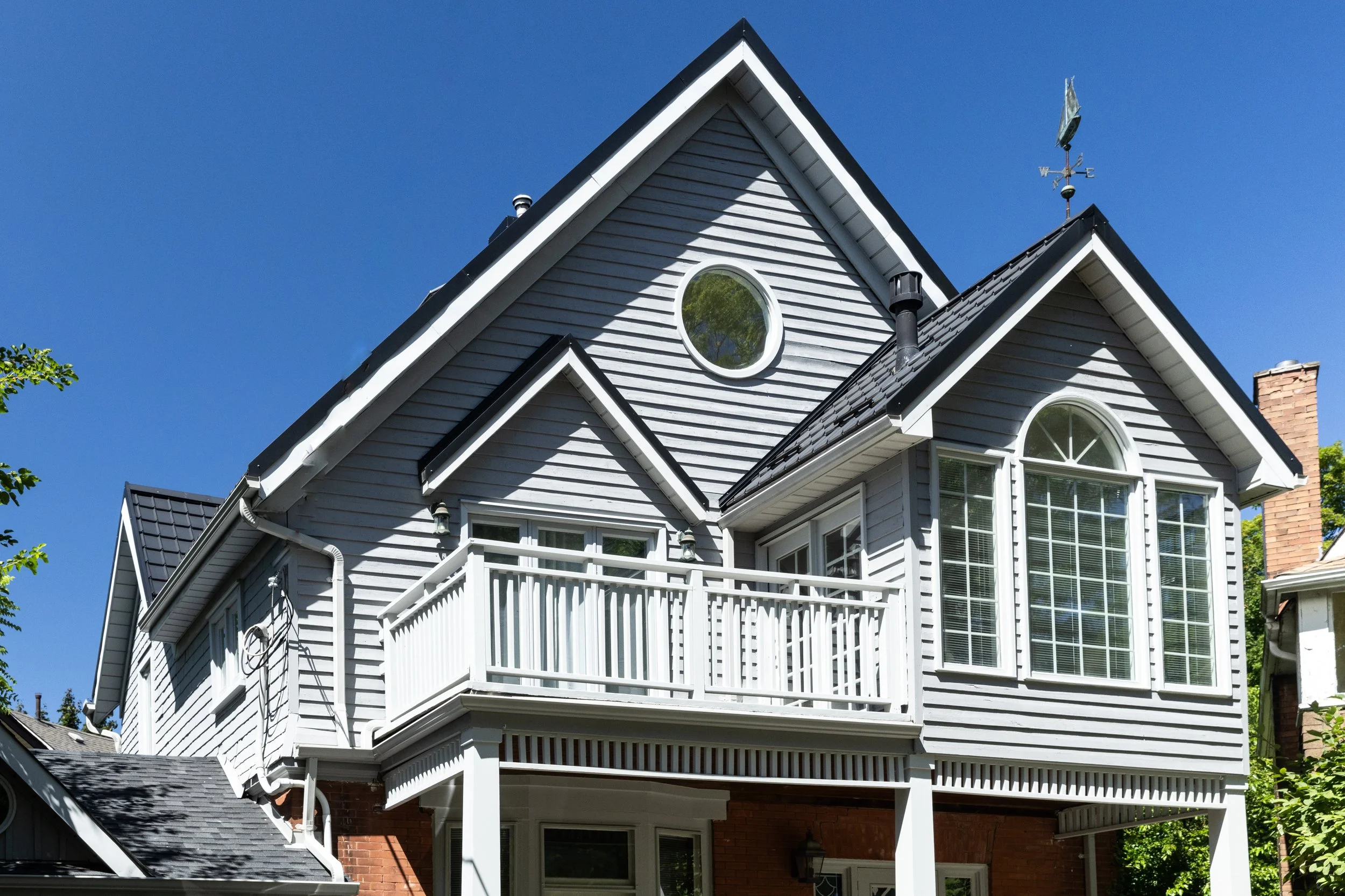 House with grey siding, white trim and balcony railings beneath steep gabled roofs