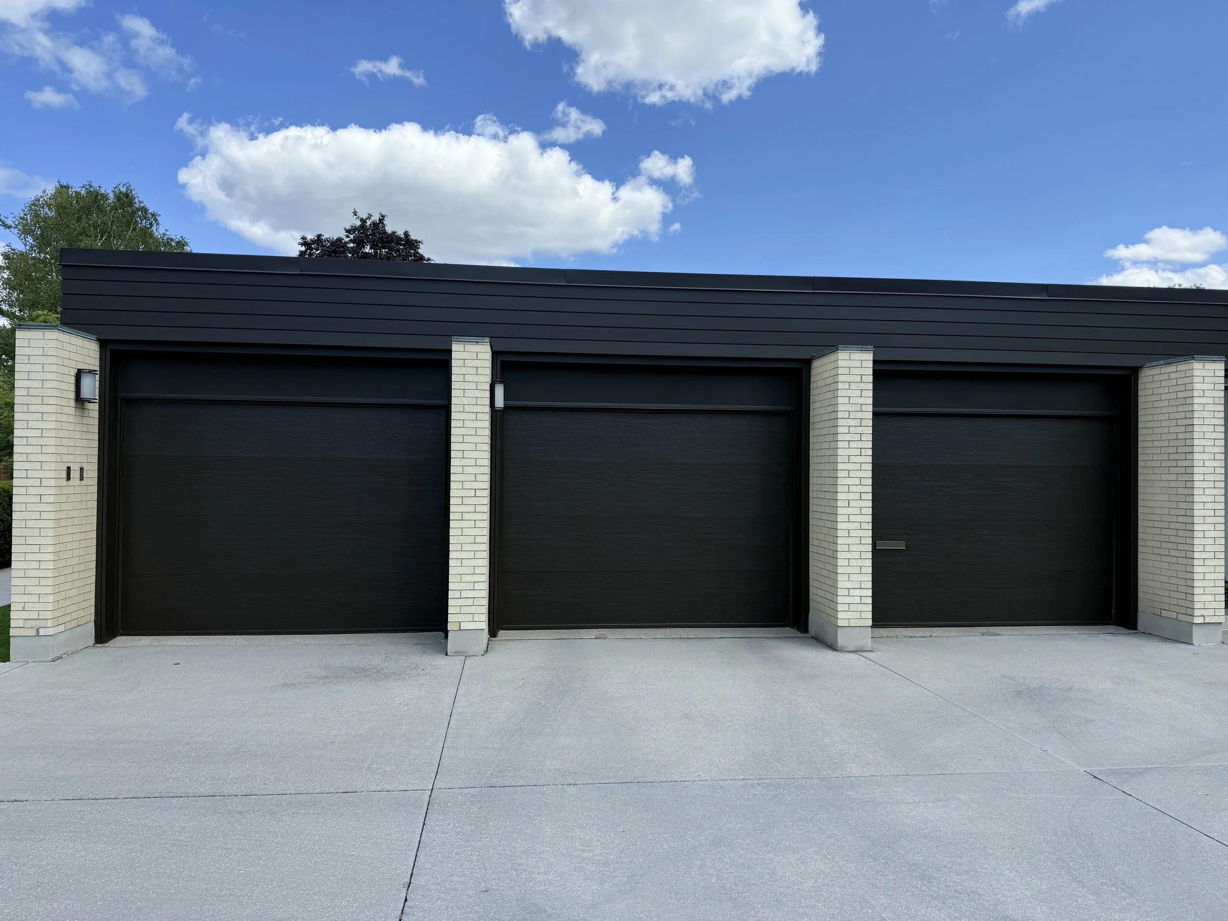 Three black garage doors with matching dark fascia and light brick surrounds