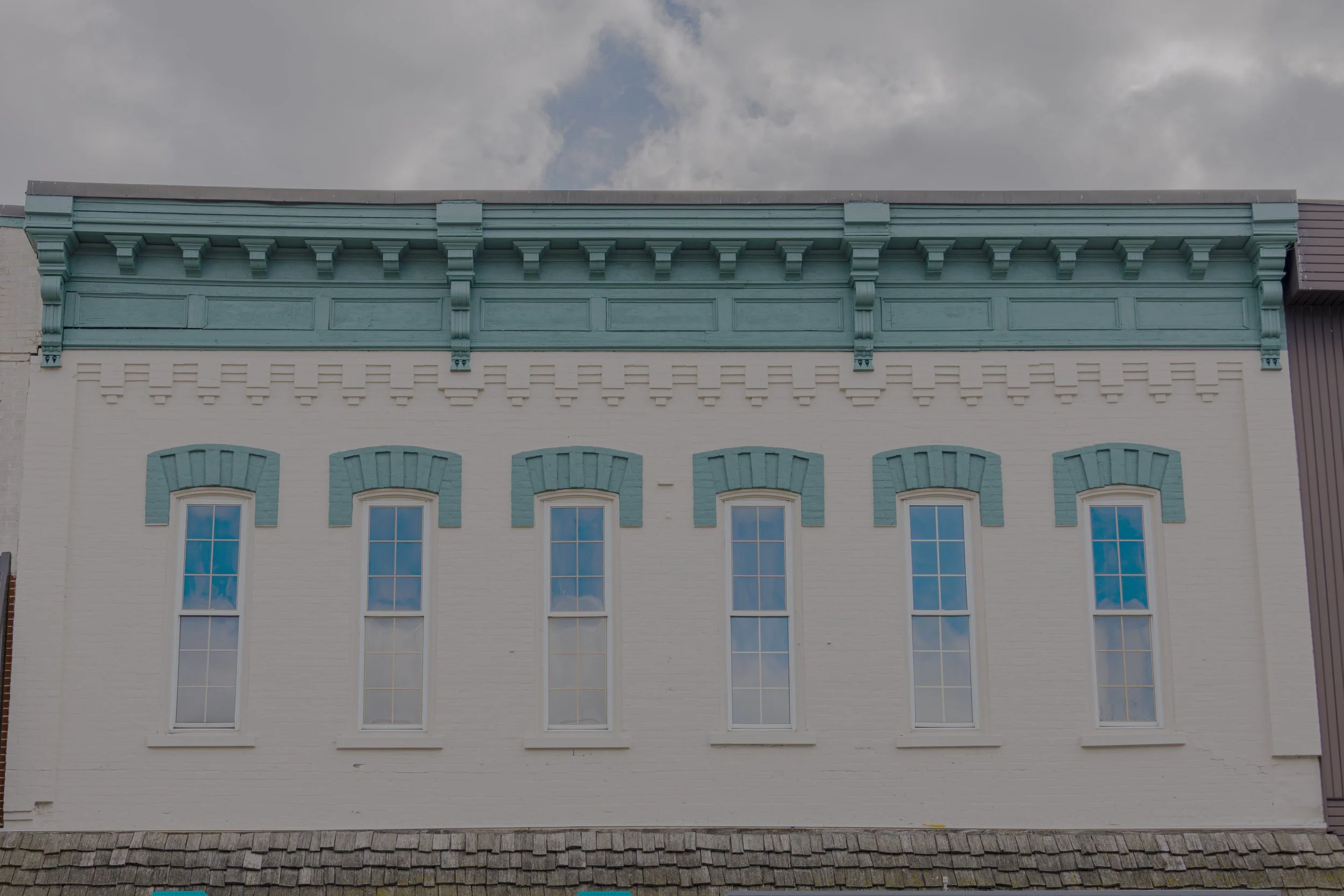 Commercial building facade with light painted brick, teal decorative cornice and matching window accents