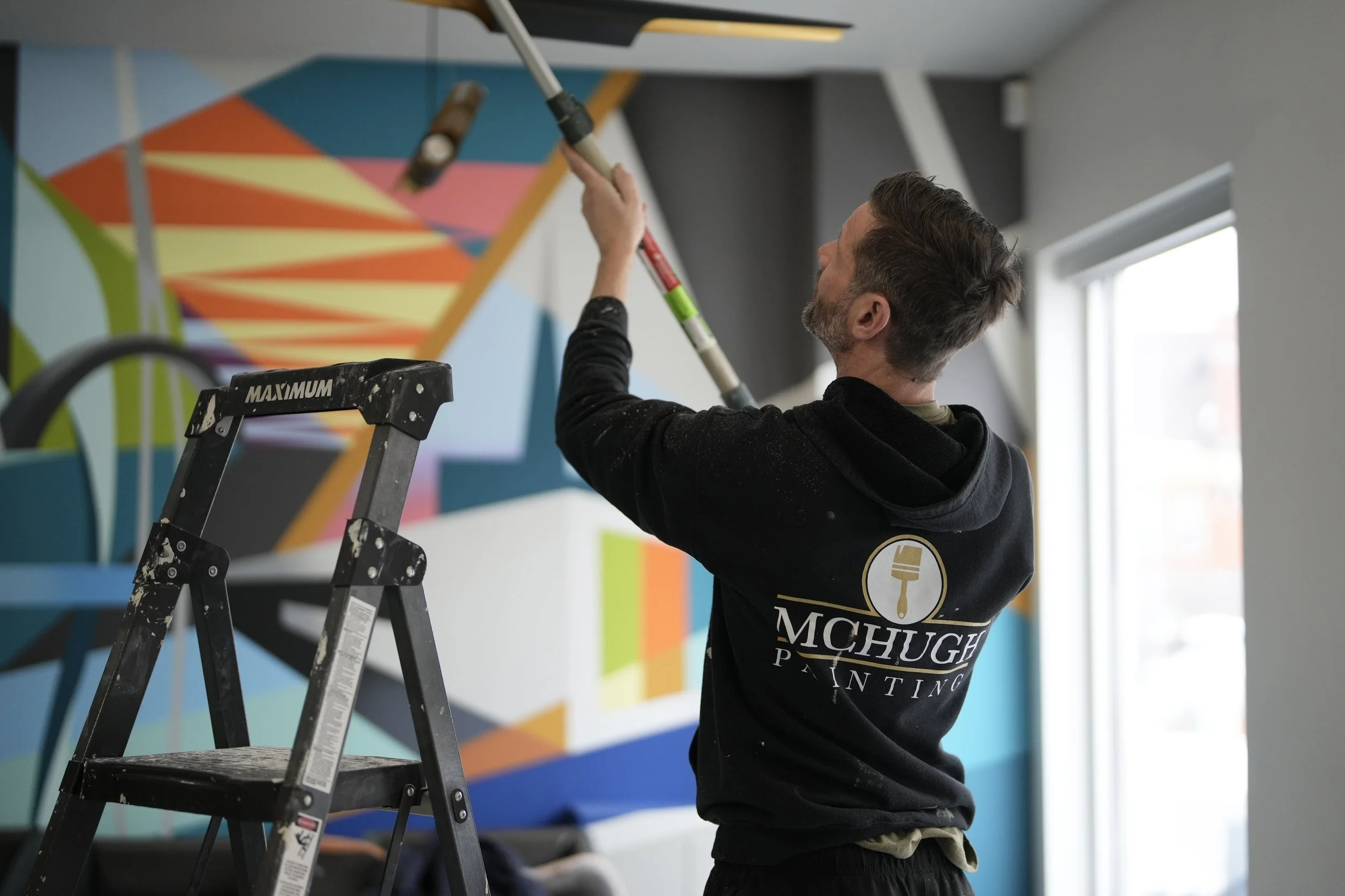 McHugh Painting crew member using an extension-pole roller to paint a ceiling beside a stepladder