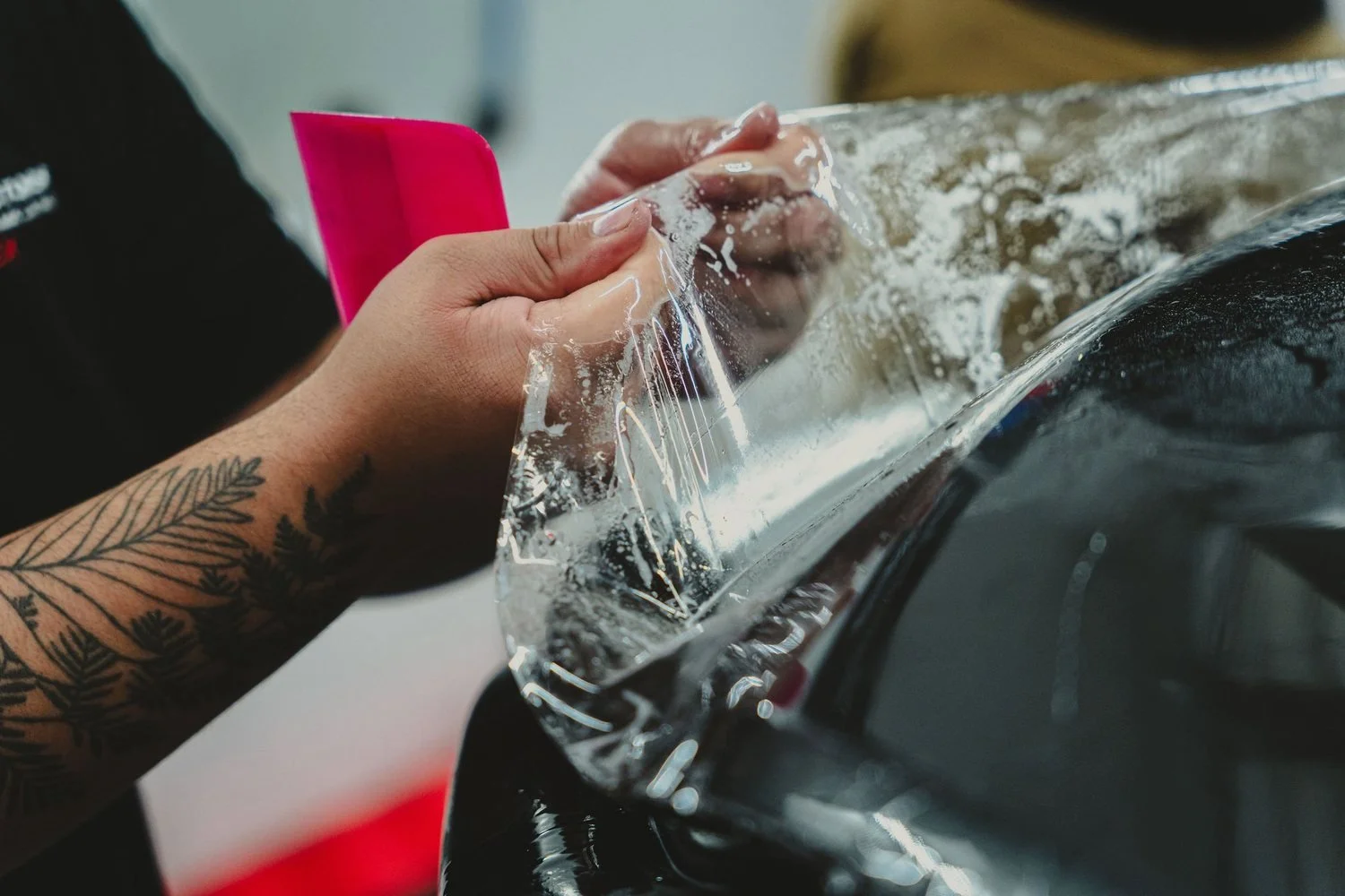 Detail Doctors installer hand-fitting PurePPF Crystal Series film around a vehicle panel edge