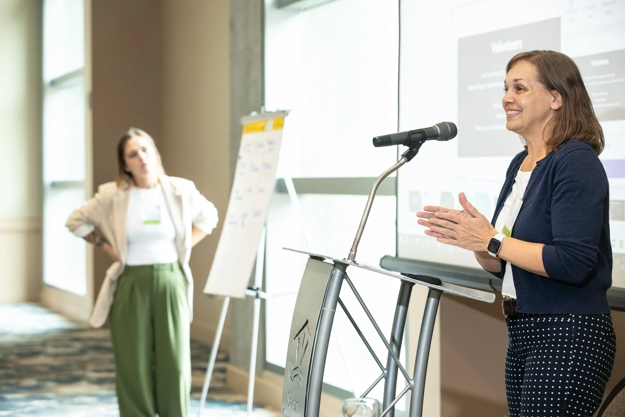 Presenter leading a workshop session at RE:Conference 2024, with whiteboard and large windows behind her