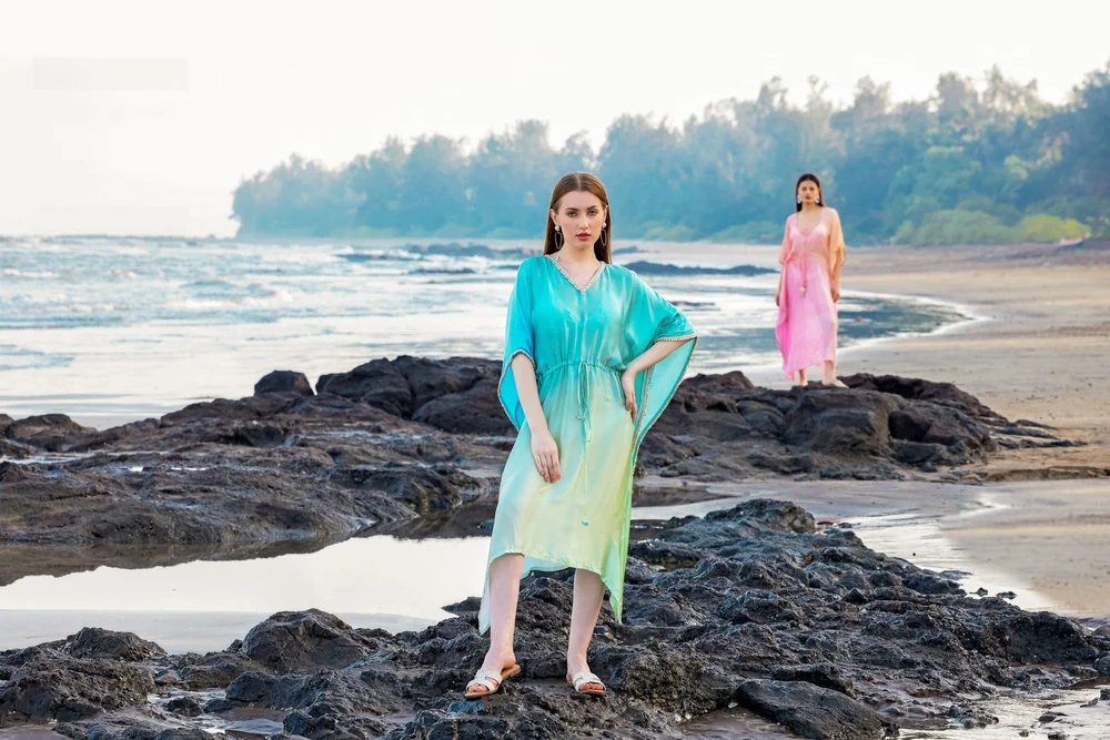 Ocean Jade Kaftan in the foreground on coastal rocks, with Sunset Rose Kaftan in the distance.