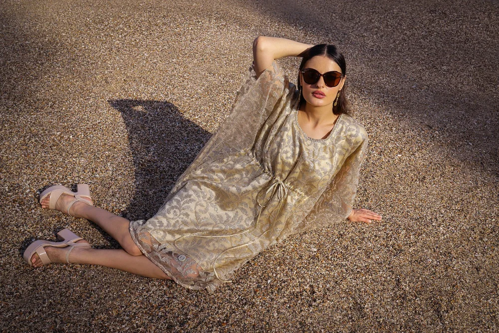 Goldleaf Oasis Kaftan worn seated on the beach, showing its patterned surface.
