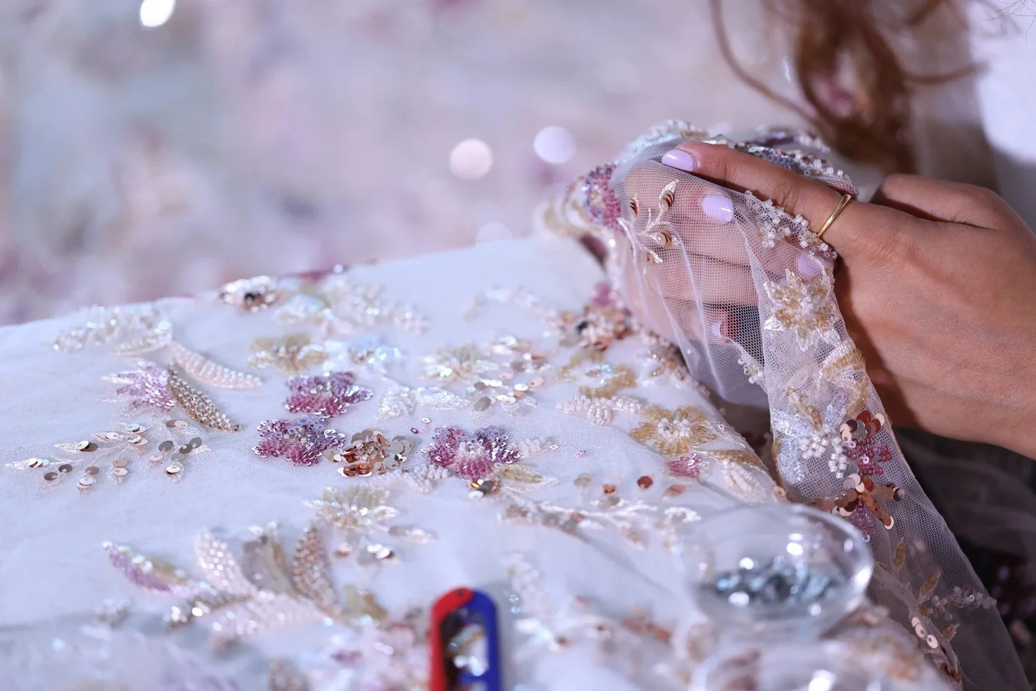 Close view of an artisan holding the sheer floral fabric and its beaded edge during hand finishing.