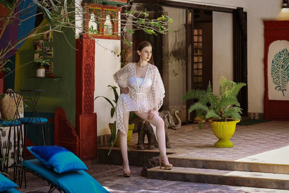 Diamond Dewdrops Kaftan worn seated in a courtyard, with its sheer geometric surface visible.