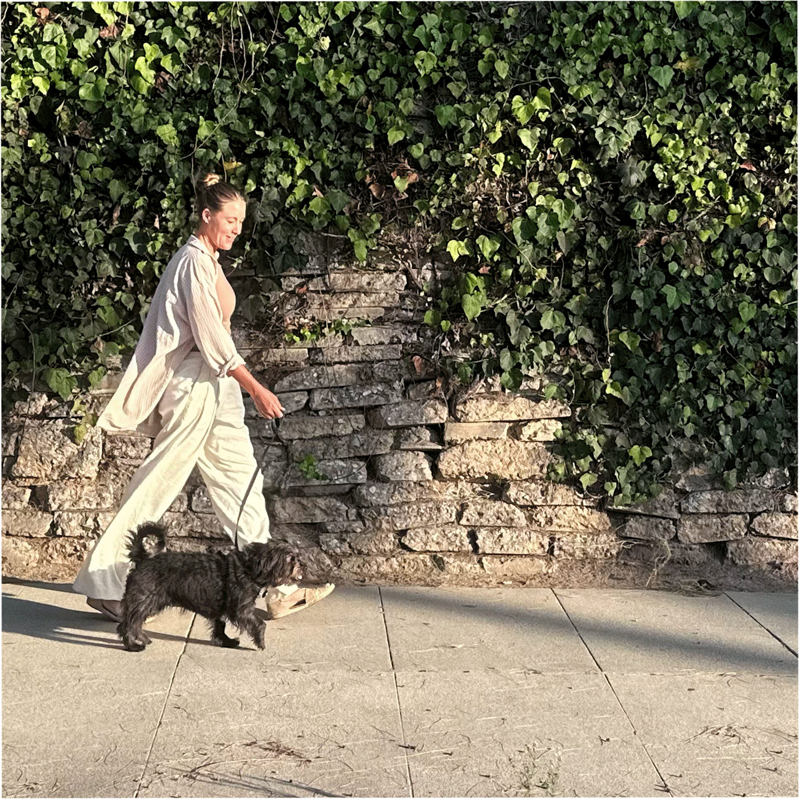 Celeste walking her dog past an ivy-covered stone wall