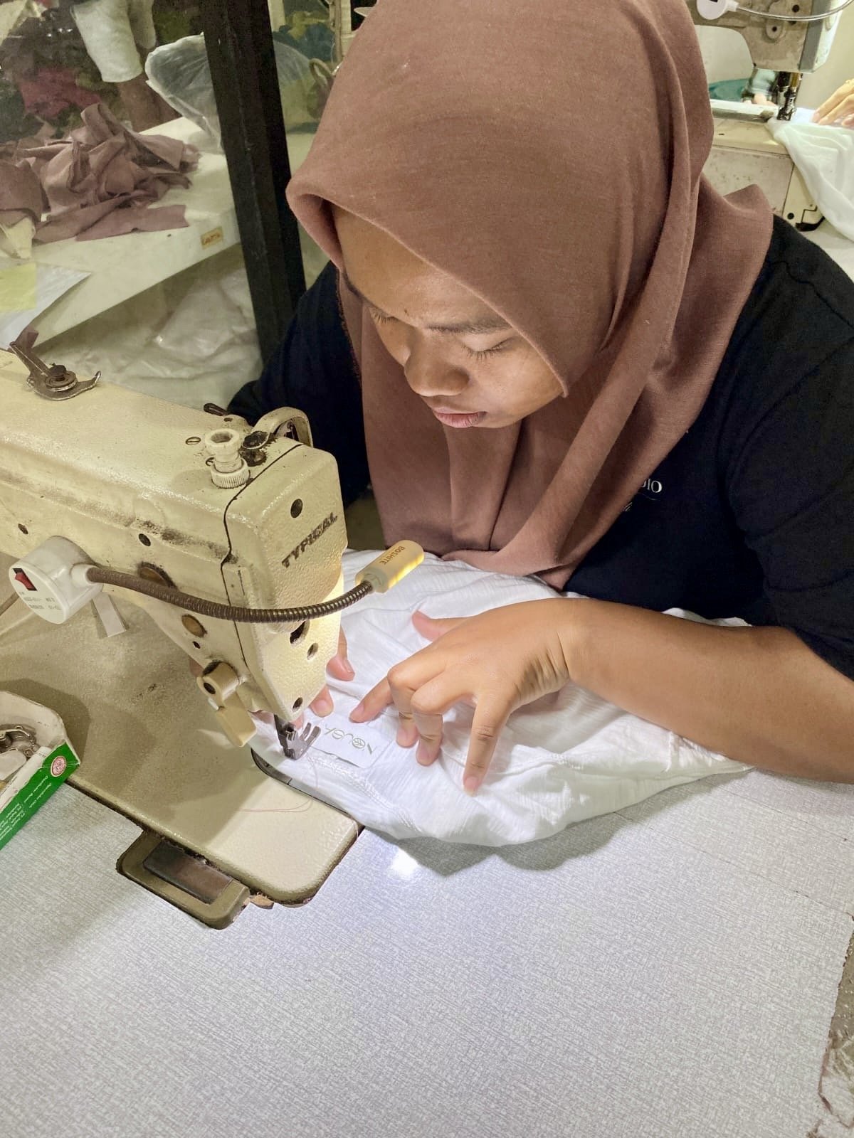 Seamstress sewing a white garment at her machine, Nousa Concept Bali workshop