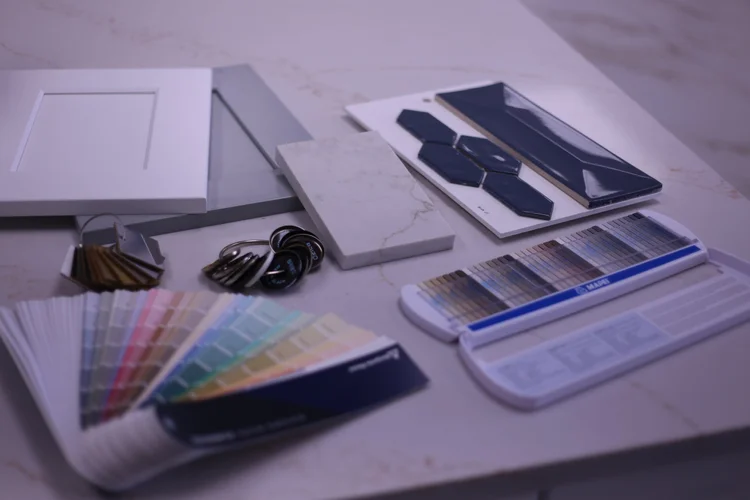 A cabinet door, quartz samples, a paint fan deck, grout colors and hardware finishes laid out on a countertop