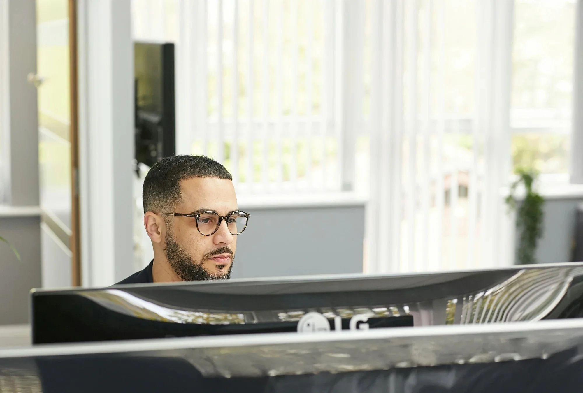 A man in glasses at his desk, looking at his monitor