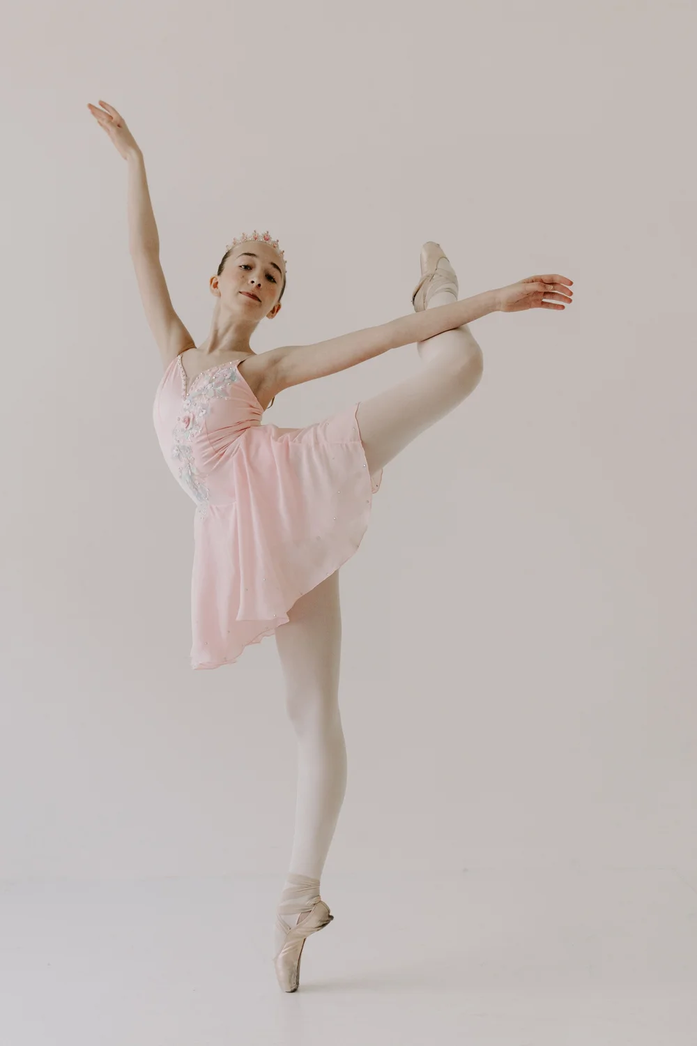 A dancer in a pink costume and tiara balancing on pointe in arabesque