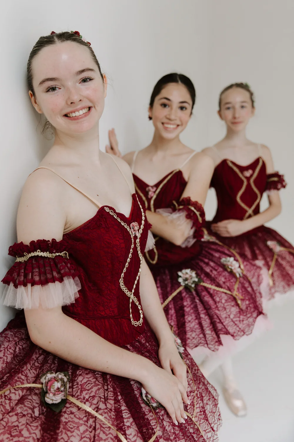 Three smiling dancers in red tutus backstage