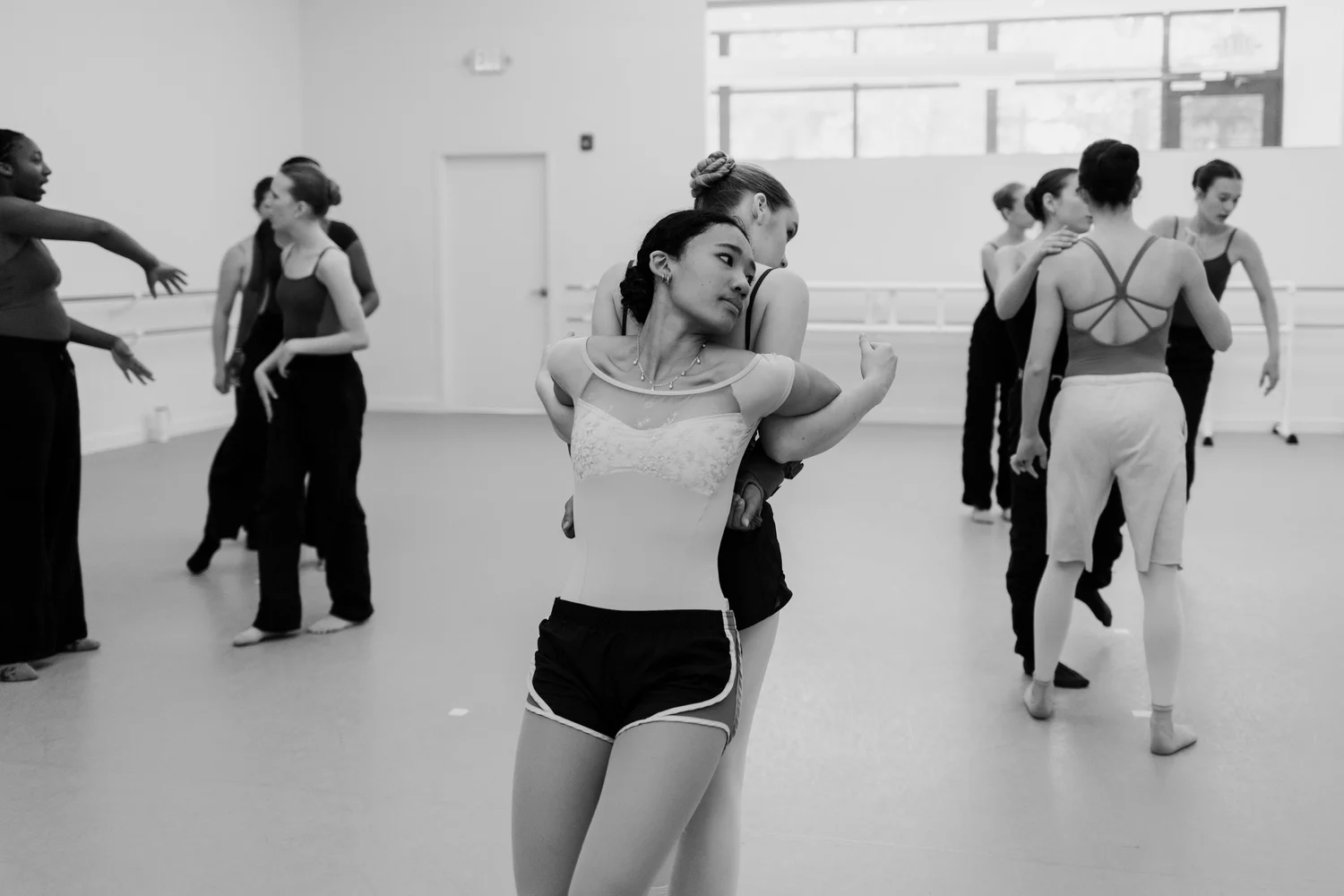 Black and white photo of company dancers working through partnering in a studio rehearsal