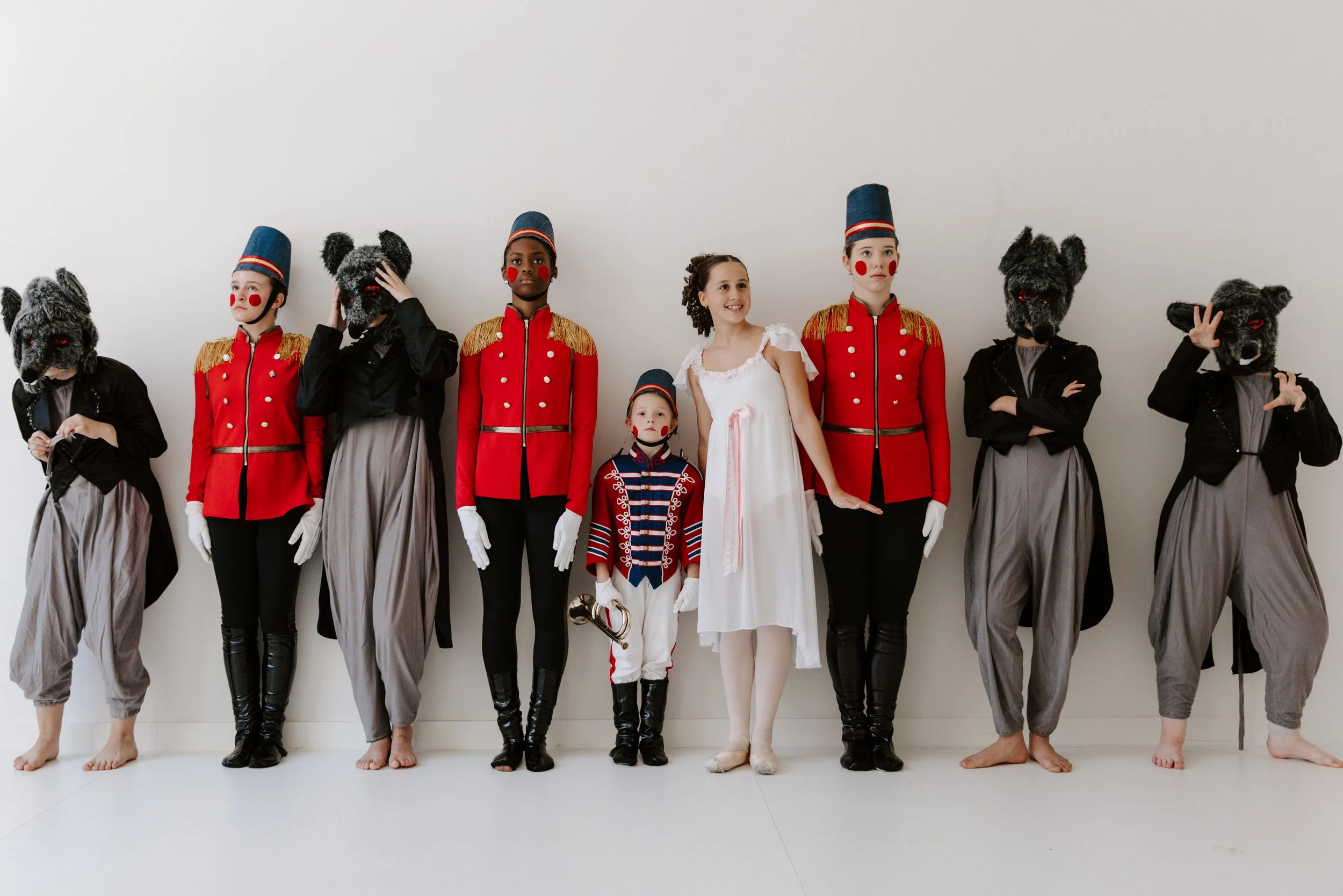 Rise City Dance company members in Nutcracker costume, soldiers, mice, Clara and a small drummer, lined up against a white studio wall