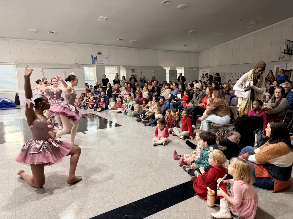 Dancers in pink tutus performing for a crowd of young children
