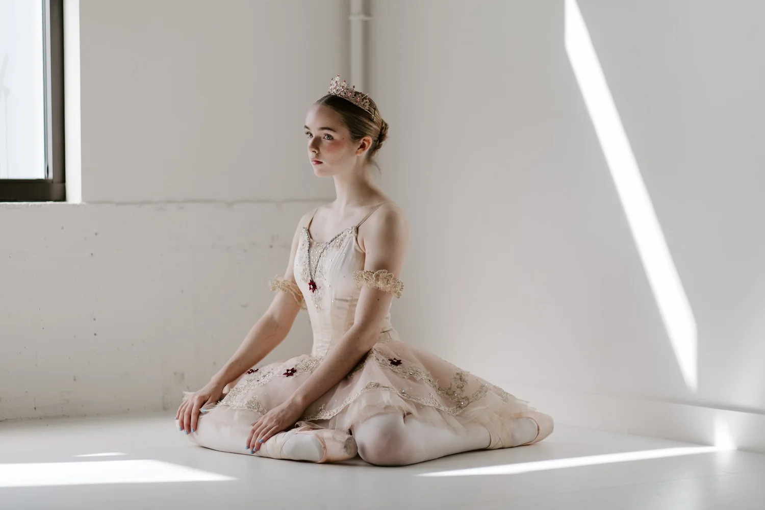 A Rise City Dance dancer in a pink tutu and tiara kneeling in window light