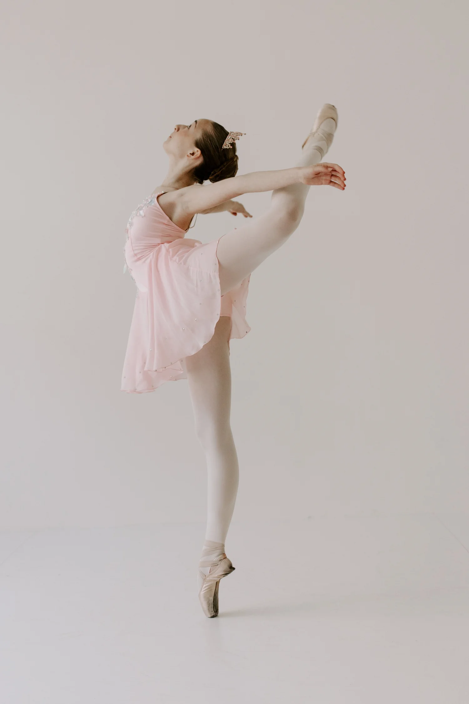 A dancer in a pink costume arching back in arabesque on pointe