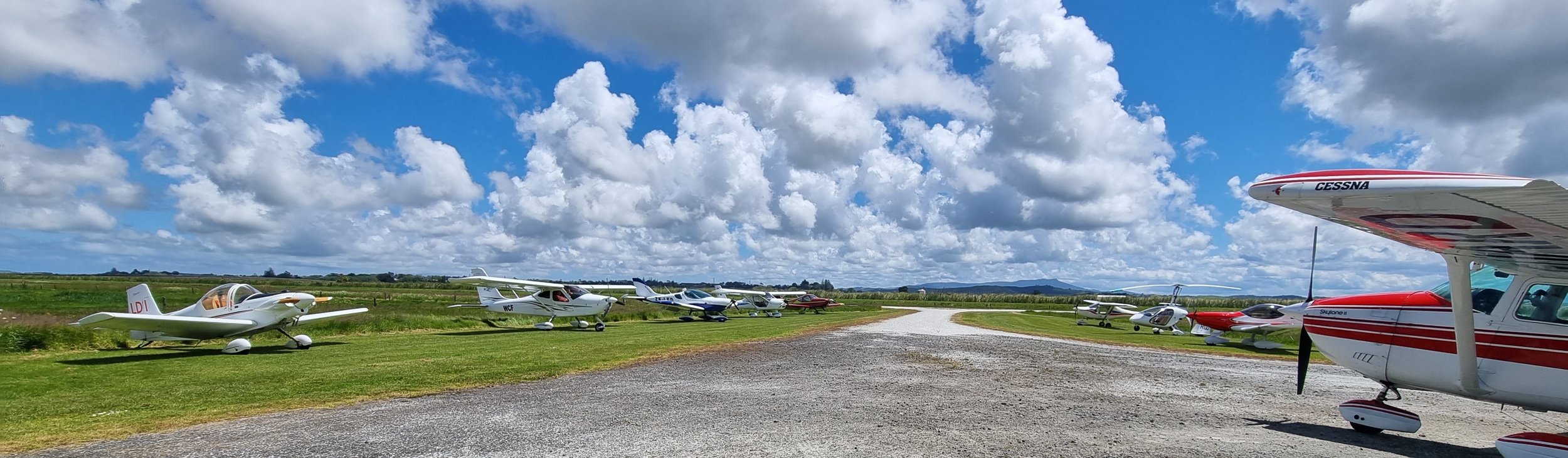 Lineup of light aircraft parked outside Dargaville Aero Club on a sunny day in Northland, New Zealand, with Cessna and other recreational planes visible under a scenic sky.