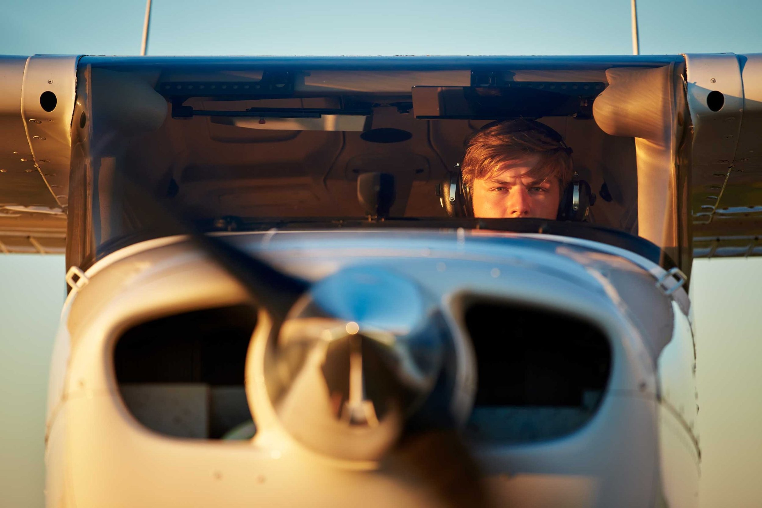 Young pilot with headphones focused on flying, seated in a small aircraft cockpit with the clear New Zealand sky ahead.