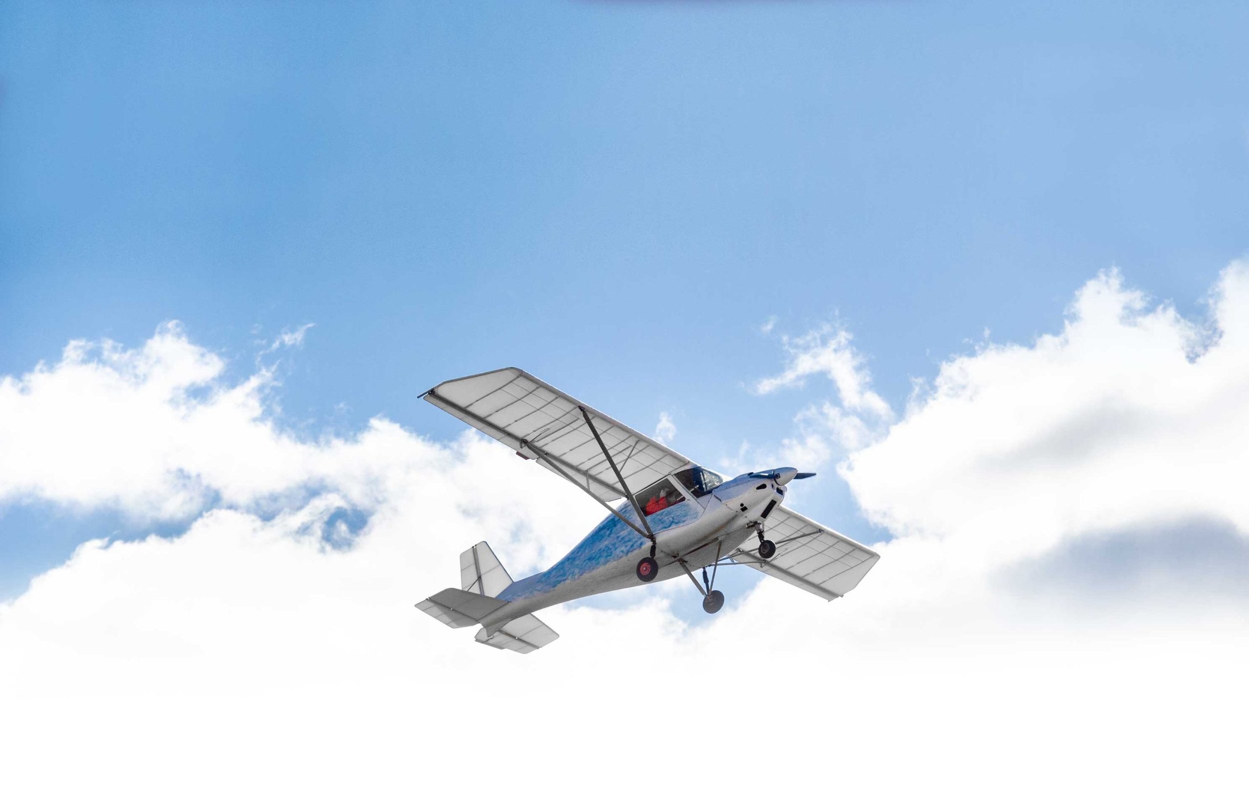 Small single-engine aircraft flying overhead against a clear blue sky with a few clouds, representing New Zealand's aviation landscape.