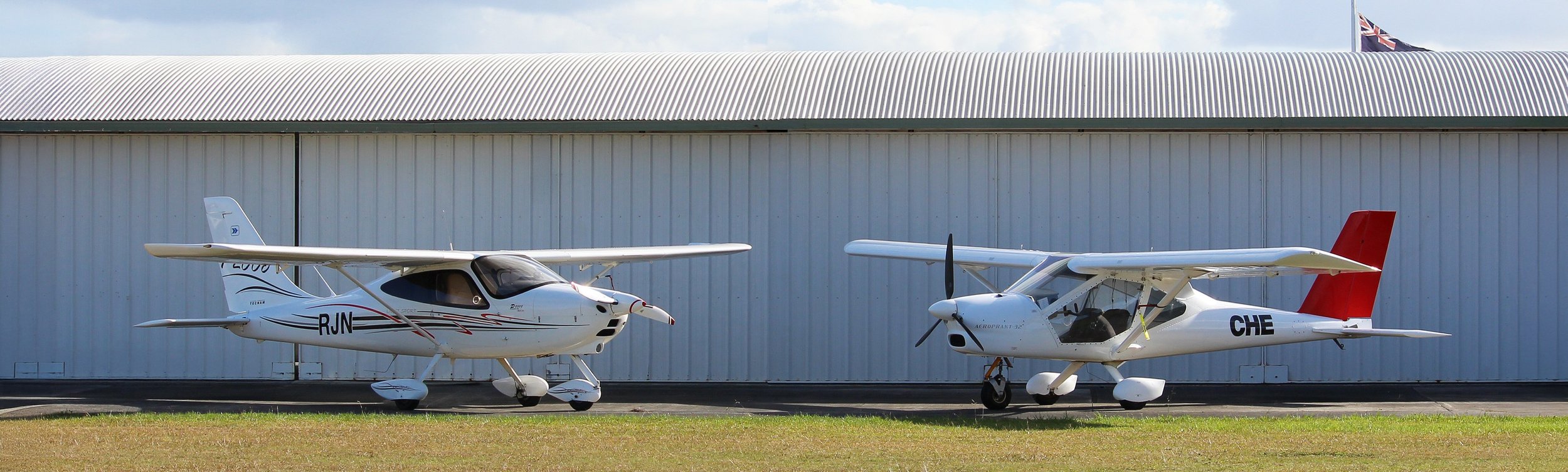 Bay of Islands Aero Club aircraft ZK-RJN (Tecnam P2008) and ZK-CHE (Aeroprakt A32 Vixxen) parked in front of the hangar at Kerikeri Airport in Northland, New Zealand.