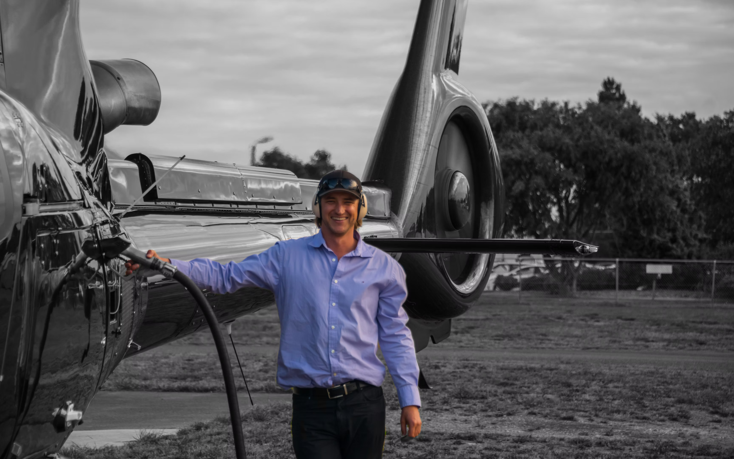 Helicopter operator smiling while fueling the aircraft, with a sleek black helicopter in the background