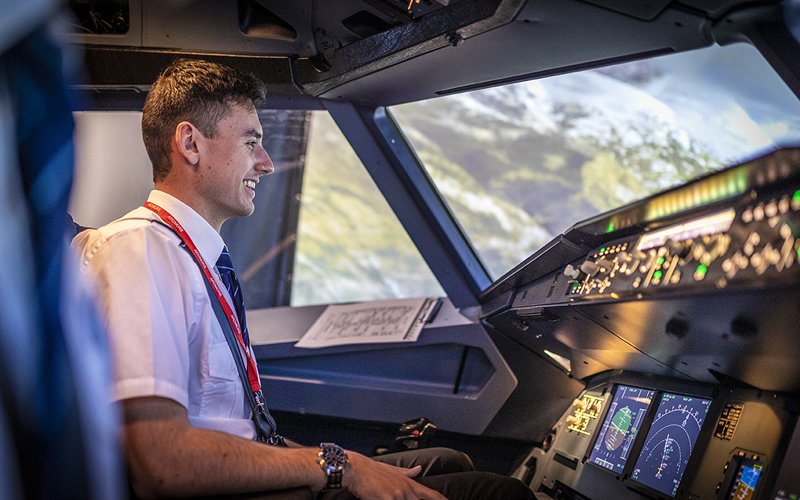 Smiling student pilot seated in a Cessna cockpit simulator at Ardmore Flying School, looking out at a virtual sky display.