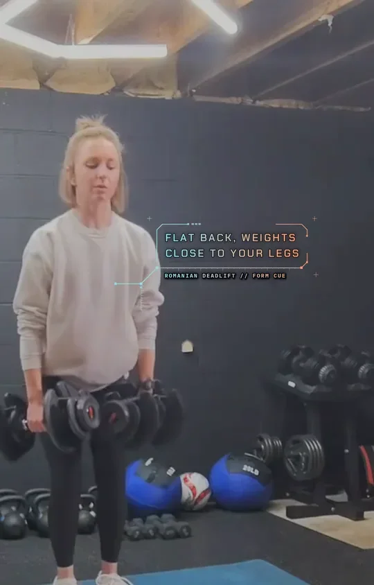 Coach Tabitha holding two dumbbells at the top of a Romanian deadlift, top: stand tall