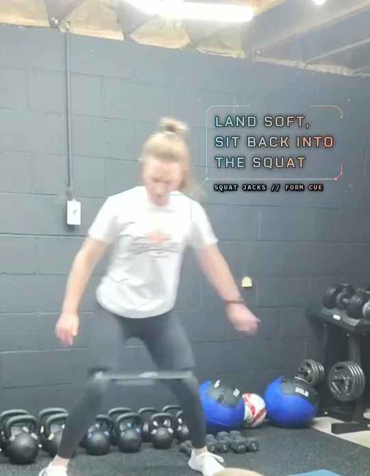 Coach Tabitha doing banded squat jacks with a mini band above her knees, jump out wide