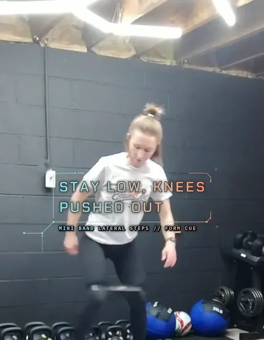 Coach Tabitha doing mini band lateral steps, mini band above her knees, step wide