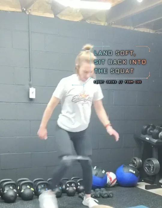 Coach Tabitha doing banded squat jacks with a mini band above her knees, start: low squat, feet in